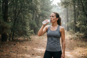 Femme en trail buvant à une flasque souple pendant l'effort en forêt